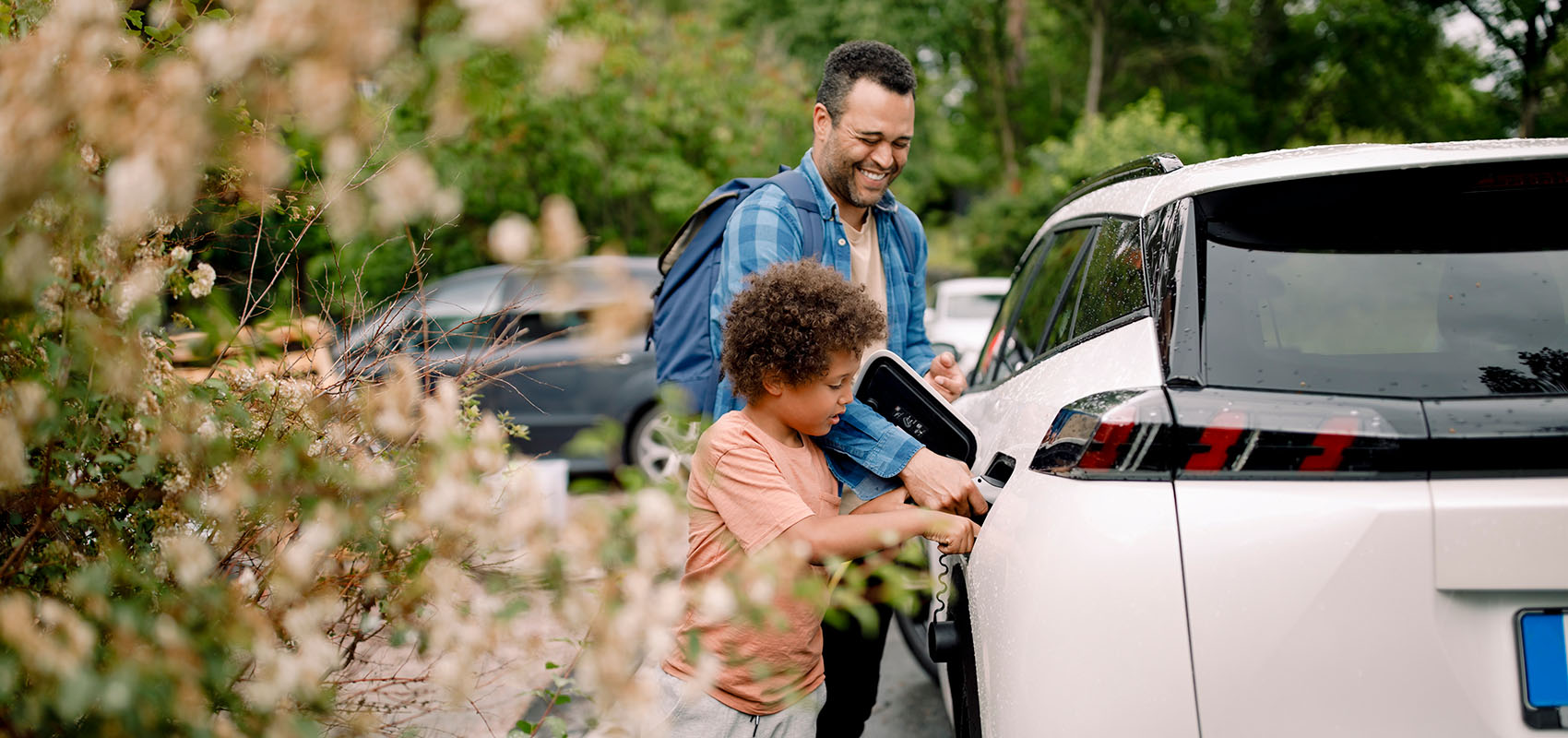 Father and son attaching charging cable to electric vehicle