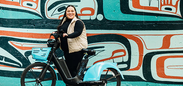 Person standing with Evolve e-bike in front of Indigenous teal mural art
