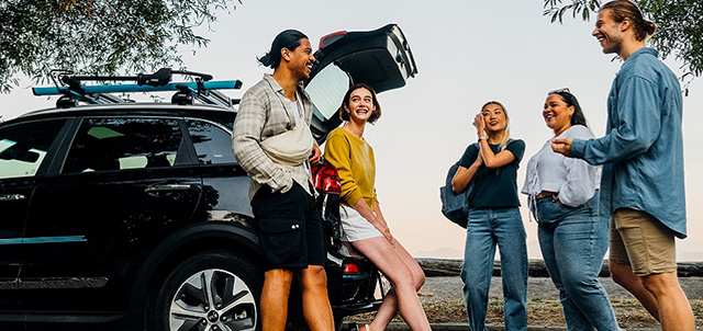 Friends gathered around trunk of an Evo at a beach at sunset