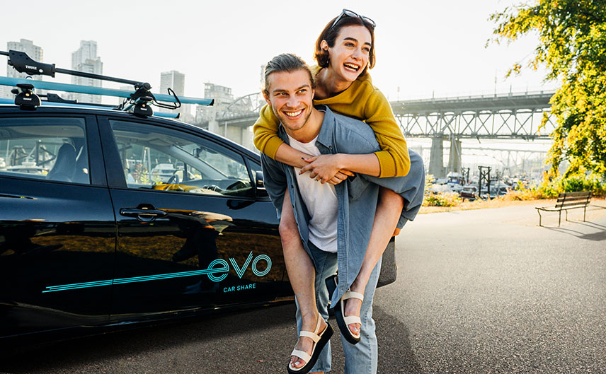 Happy friends with parked Evo car, enjoying car sharing